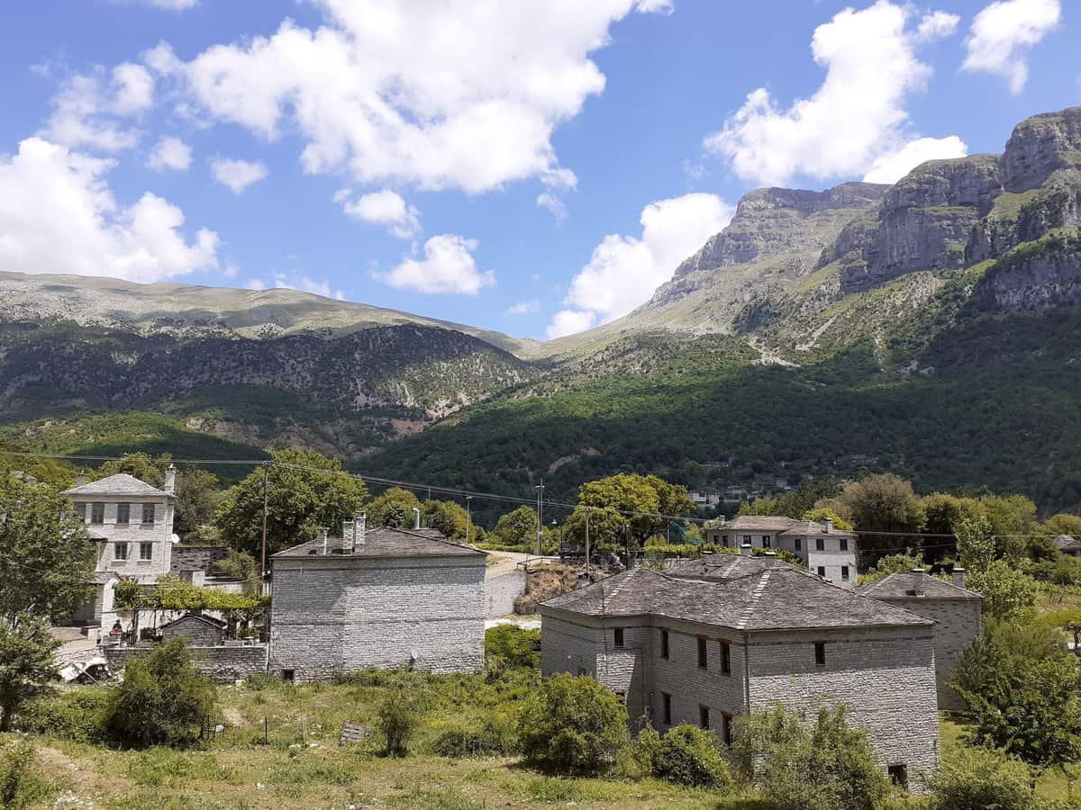 Πέτρινα σπίτια στο Μεγάλο Πάπιγκο με πράσινο κάμπο, γαλάζιο ουρανό και τα βράχια της Αστράκας